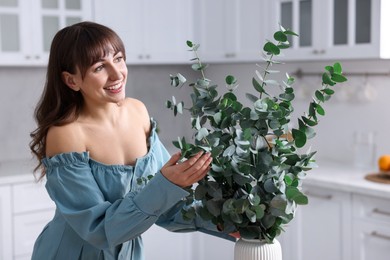 Woman with green eucalyptus branches in kitchen