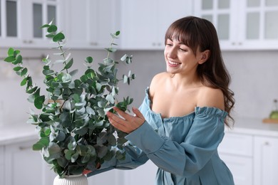 Photo of Woman with green eucalyptus branches in kitchen