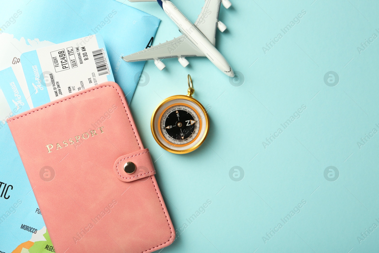 Photo of Passport with tickets, plane model, map and compass on light blue background, flat lay. Space for text