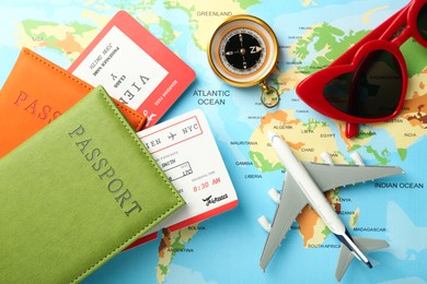 Photo of Passport with tickets, compass, sunglasses and plane model on world map, flat lay