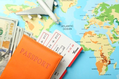 Photo of Passport with tickets, money and plane model on world map, flat lay