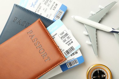 Photo of Passports with tickets, plane model and compass on light background, flat lay