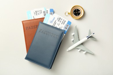 Photo of Passports with tickets, plane model and compass on light background, flat lay