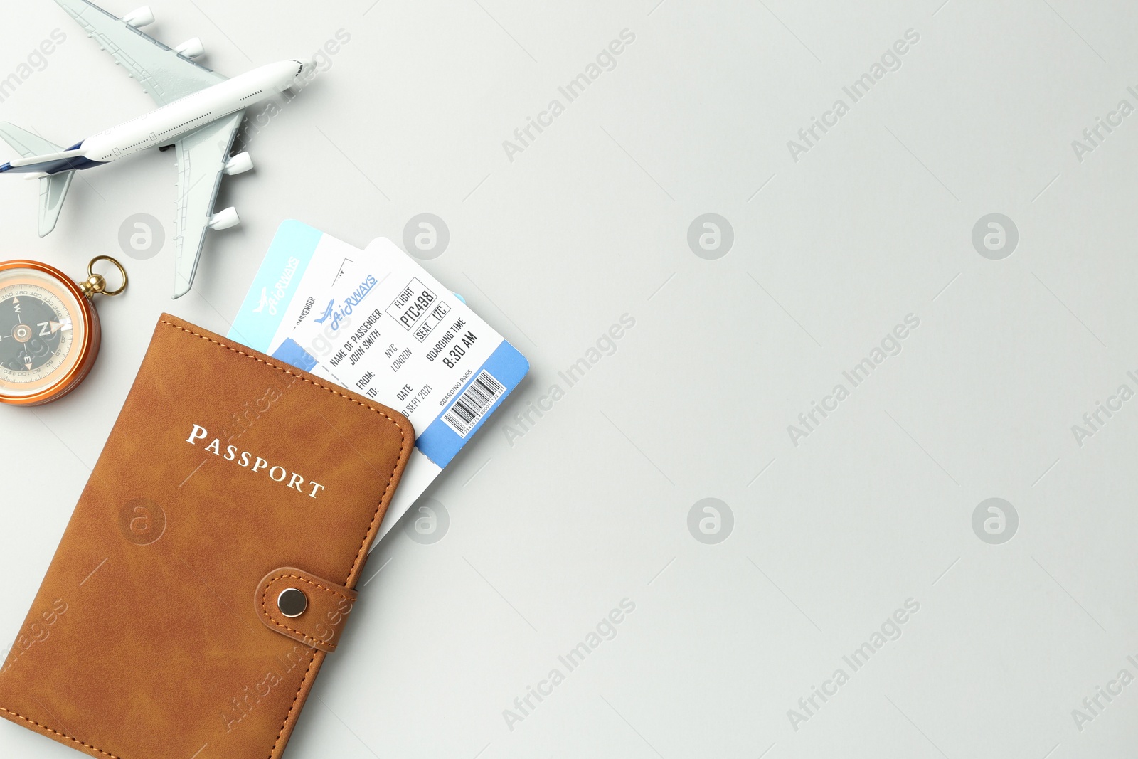 Photo of Passport in brown cover, plane model, compass and flight tickets on light grey background, flat lay. Space for text