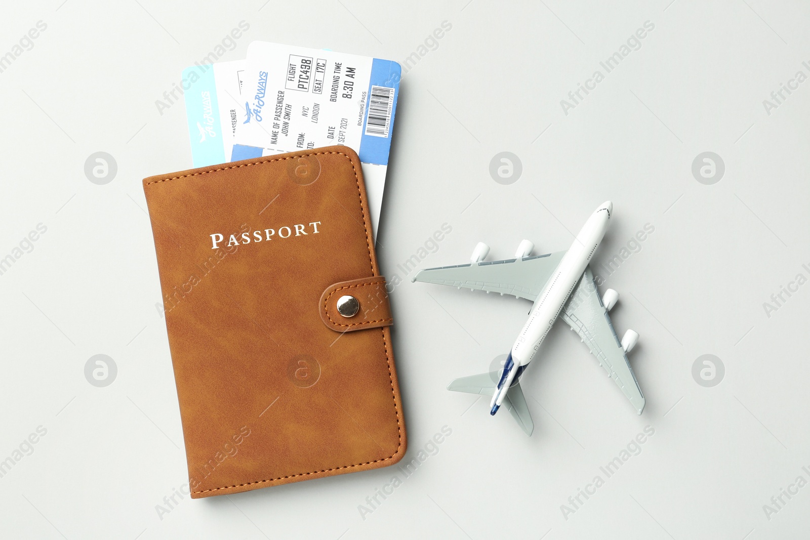 Photo of Passport in brown cover, plane model and flight tickets on light grey background, top view