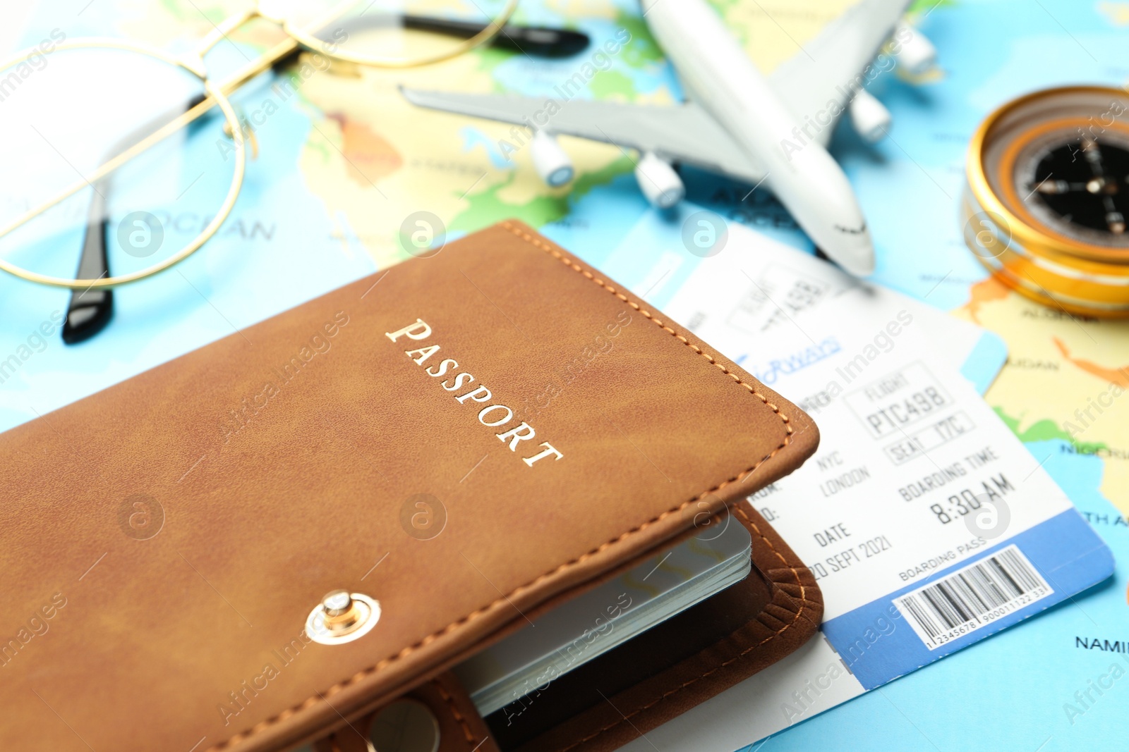 Photo of Passport in brown cover, fight tickets, plane model, compass and glasses on world map, closeup