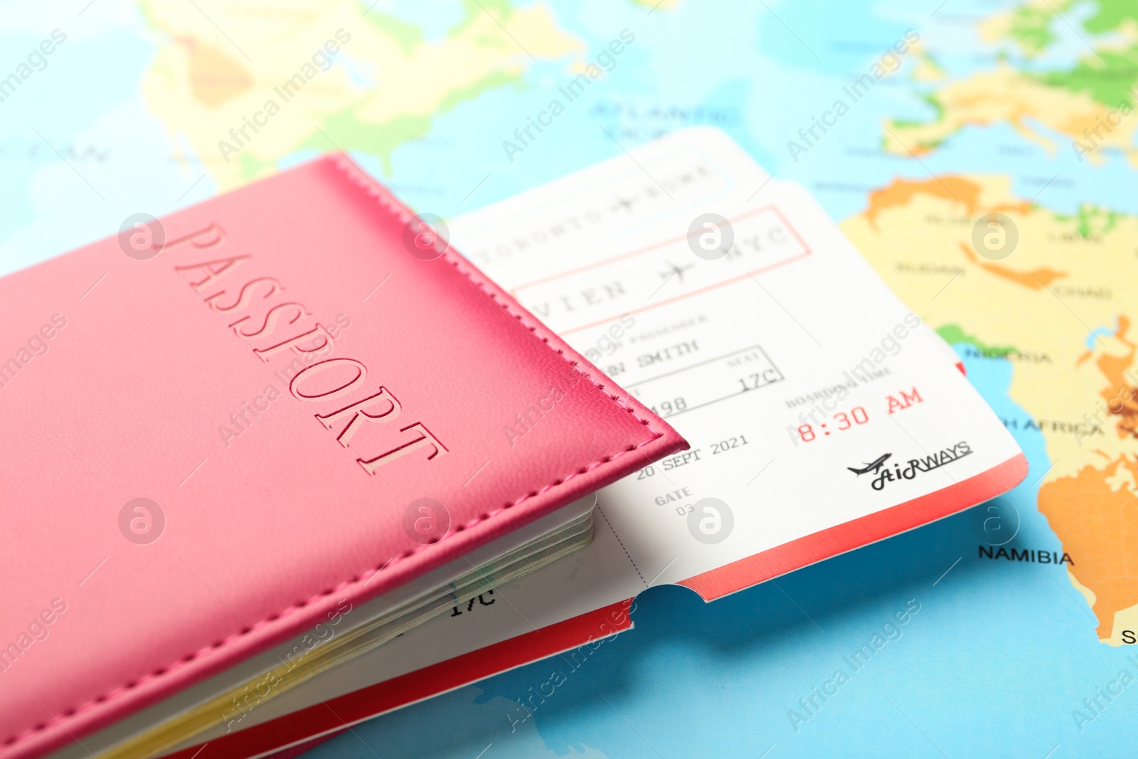 Photo of Passport in pink cover and flight tickets on world map, closeup