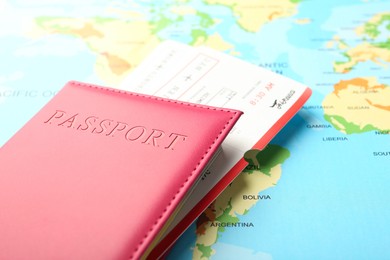 Photo of Passport in pink cover and flight tickets on world map, closeup