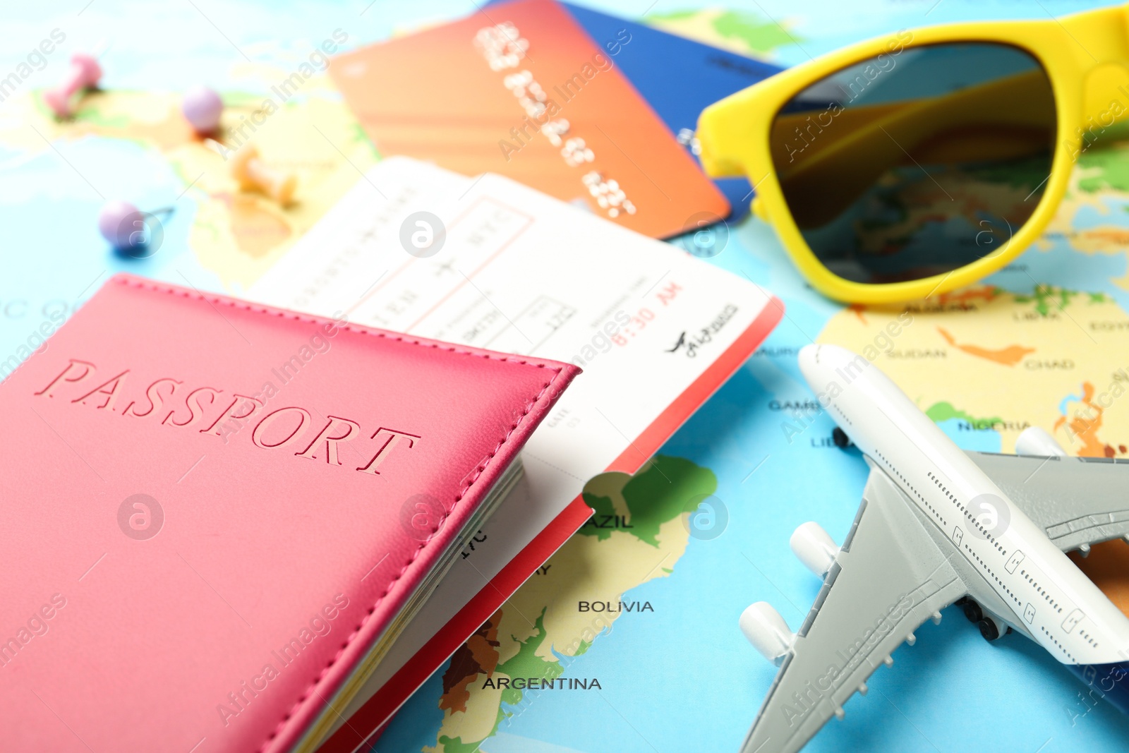 Photo of Passport in pink cover, flight tickets, sunglasses, plane model and credit cards on world map, closeup