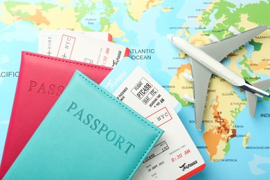 Photo of Passports in color covers, flight tickets and plane model on world map, flat lay