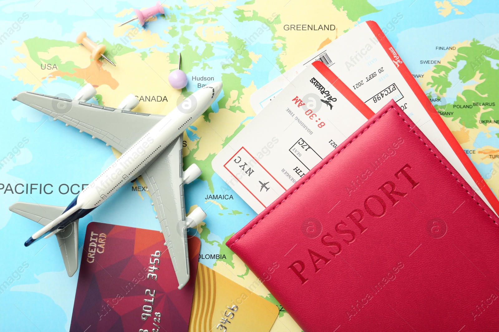 Photo of Passport in pink cover, flight tickets, plane model, drawing pins and credit cards on world map, flat lay