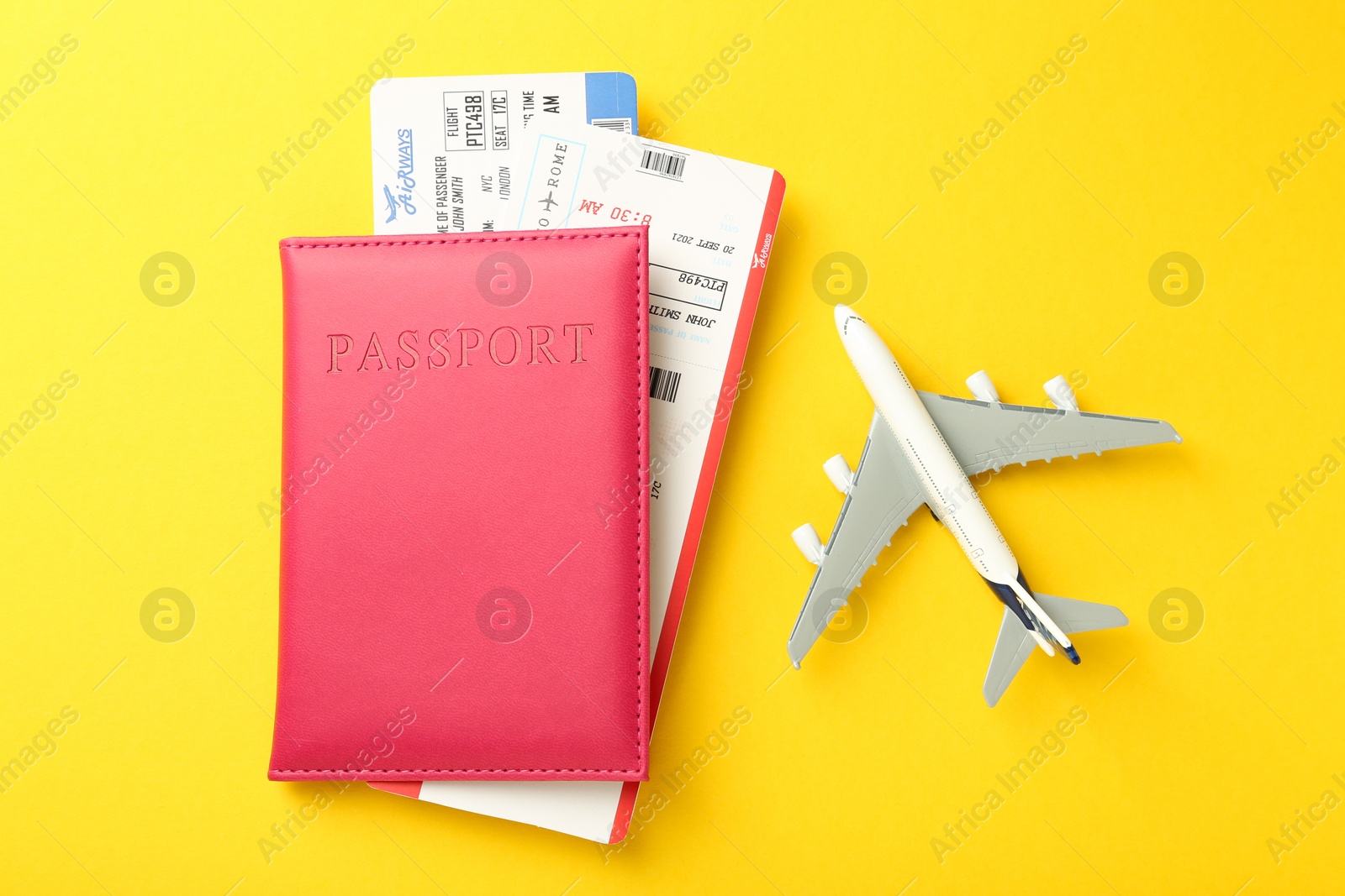 Photo of Passport in pink cover, plane model and flight tickets on yellow background, top view