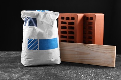 Photo of Bricks, bag of cement and wooden plank on grey table