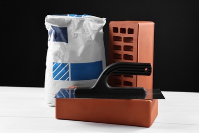 Photo of Bricks, bag of cement and construction tool on white wooden table