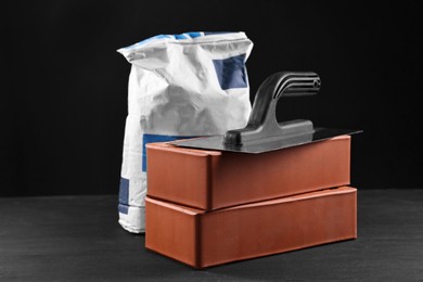 Photo of Bricks, bag of cement and construction tool on black table