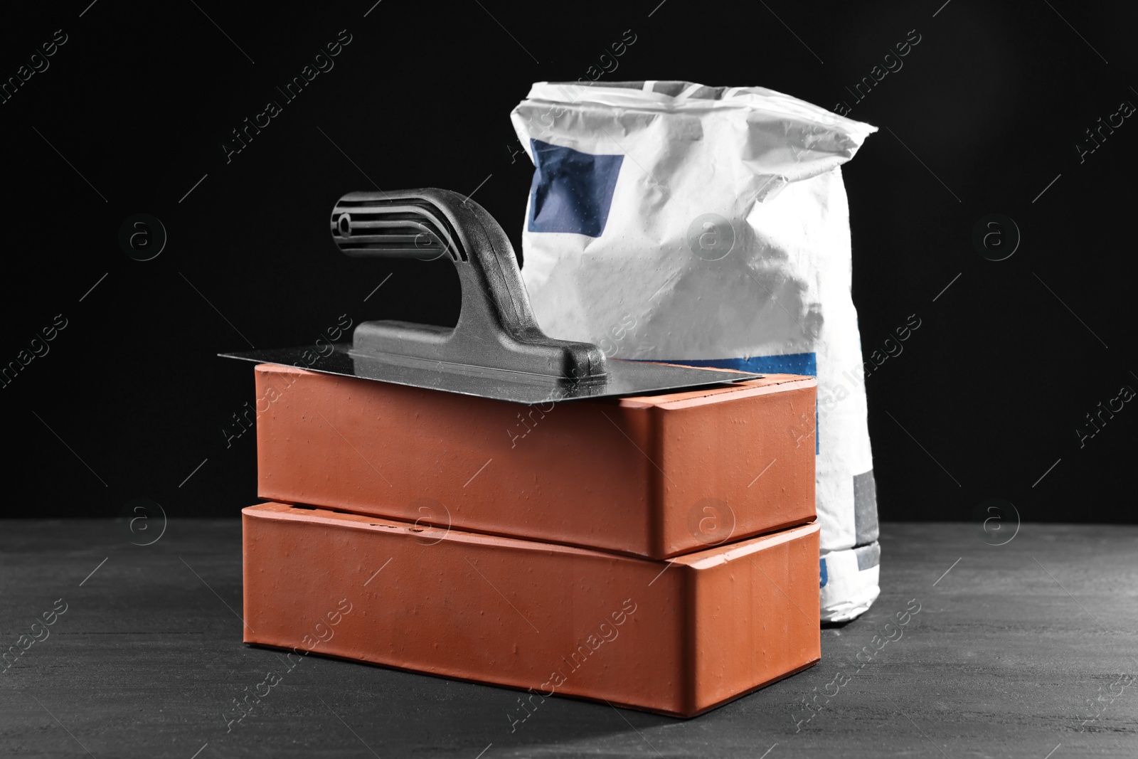 Photo of Bricks, bag of cement and construction tool on black table