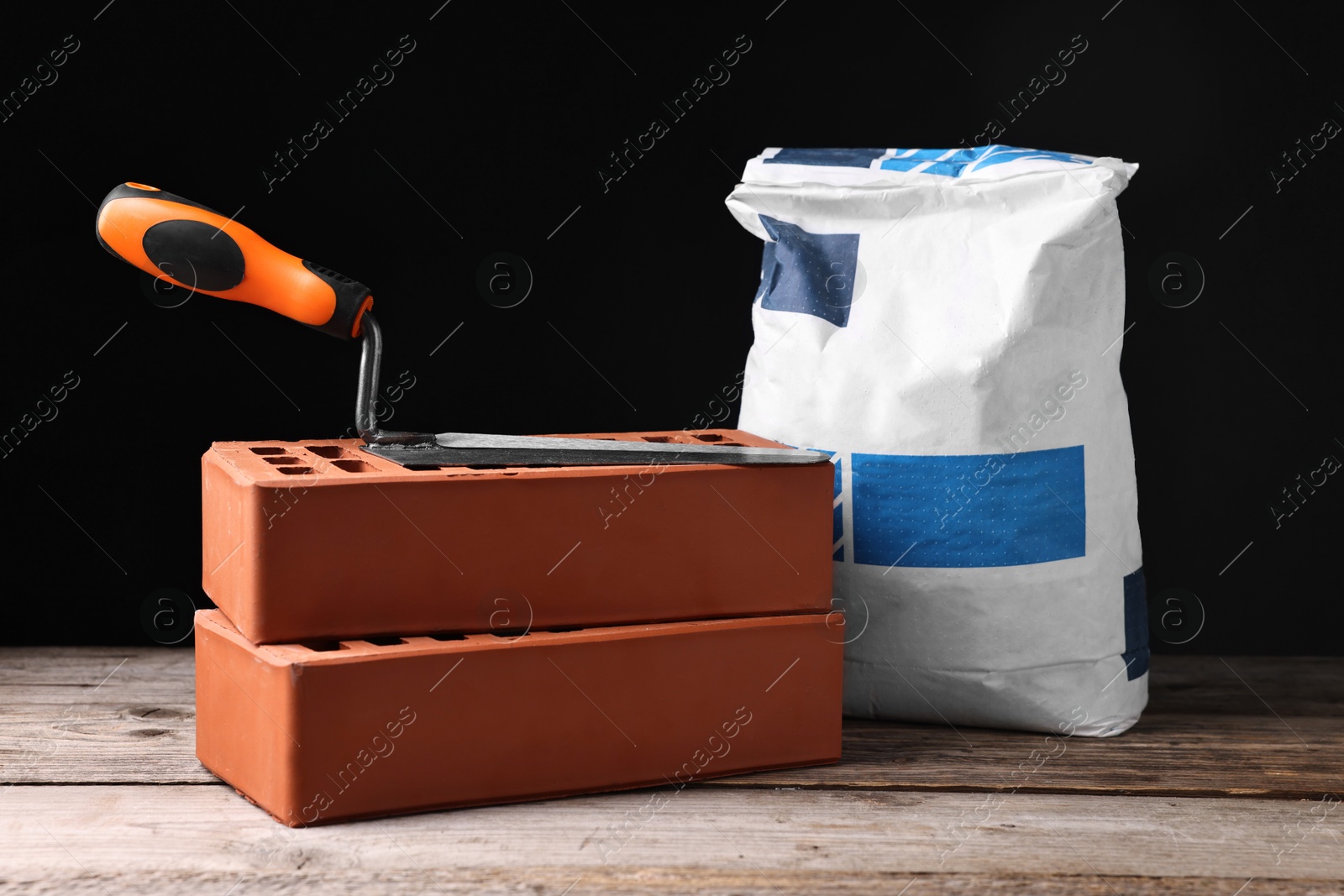 Photo of Bricks, bag of cement and bucket trowel on wooden table