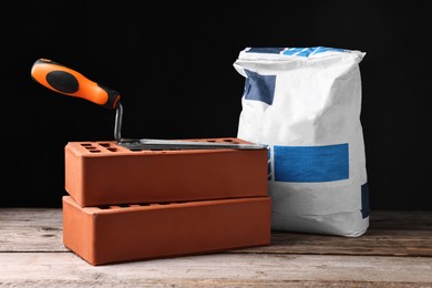 Photo of Bricks, bag of cement and bucket trowel on wooden table