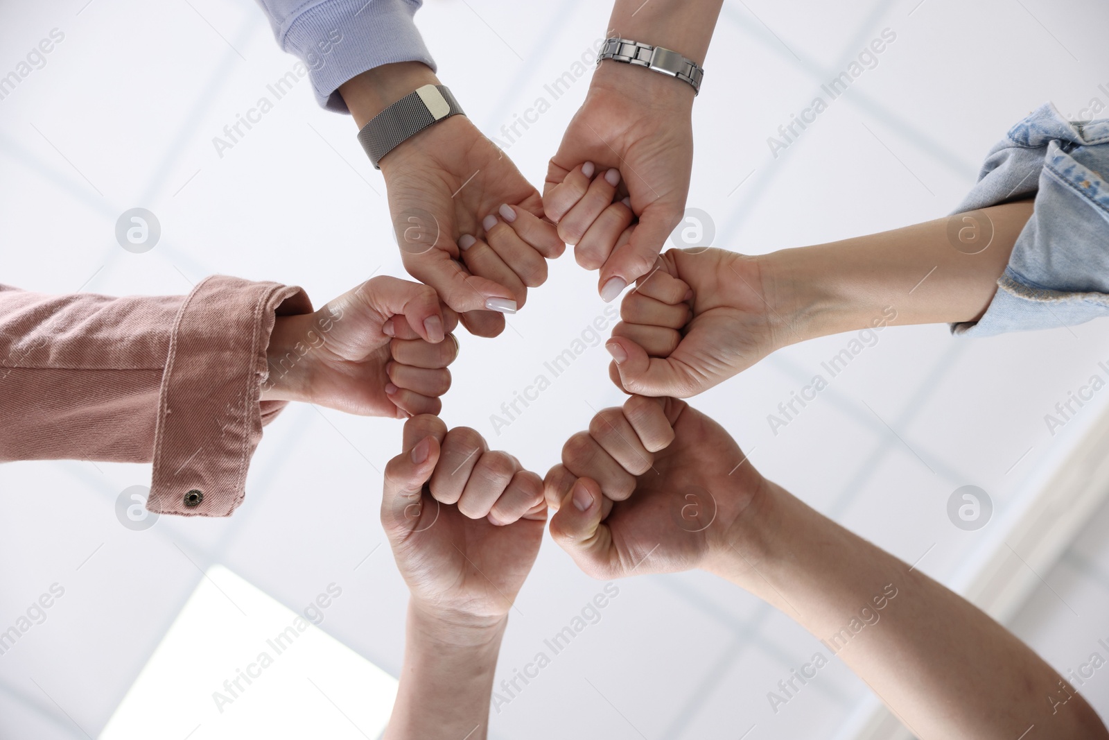 Photo of Unity concept. People holding fists together indoors, bottom view