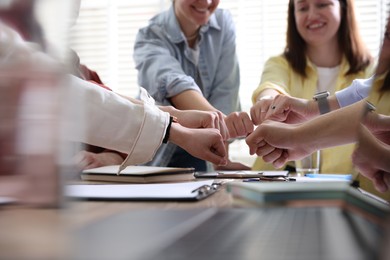 Unity concept. People holding fists together at table indoors, closeup