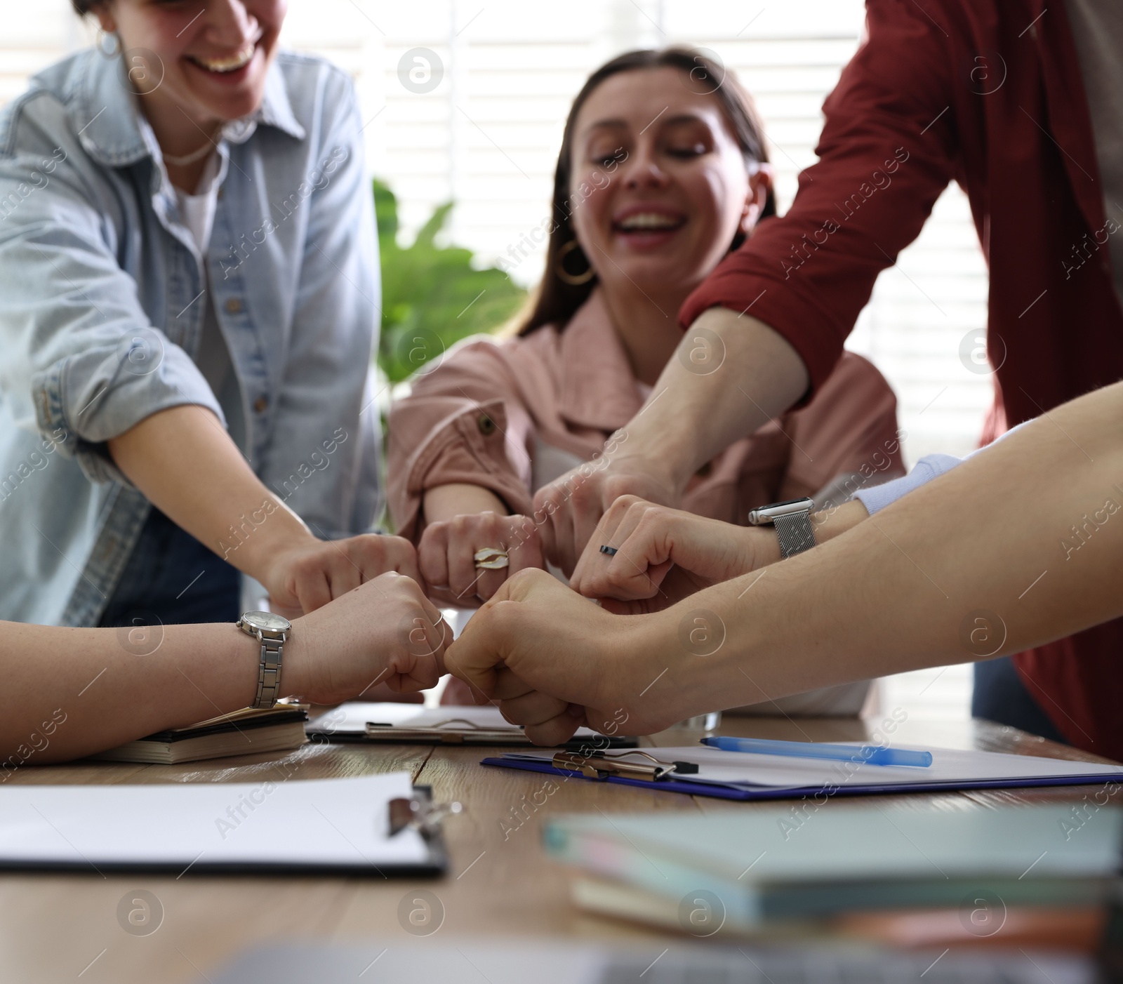 Photo of Unity concept. People holding fists together at table indoors, closeup