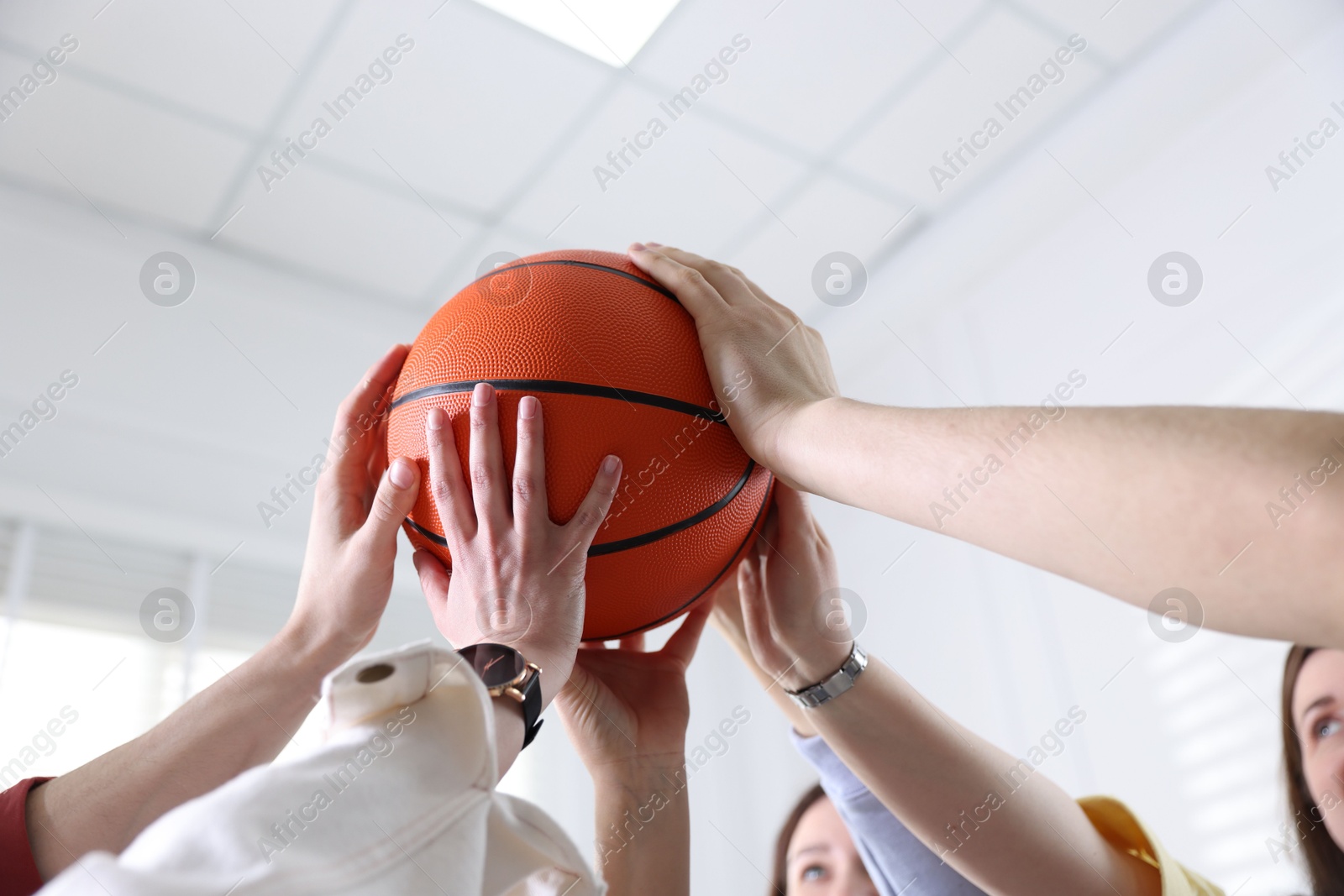 Photo of Unity concept. People holding basketball ball together indoors, low angle view