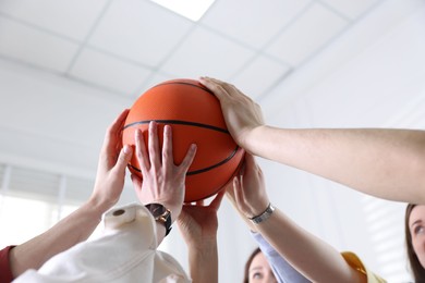 Unity concept. People holding basketball ball together indoors, low angle view