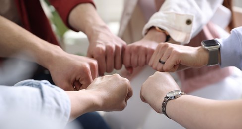 Photo of Unity concept. People holding fists together indoors, closeup