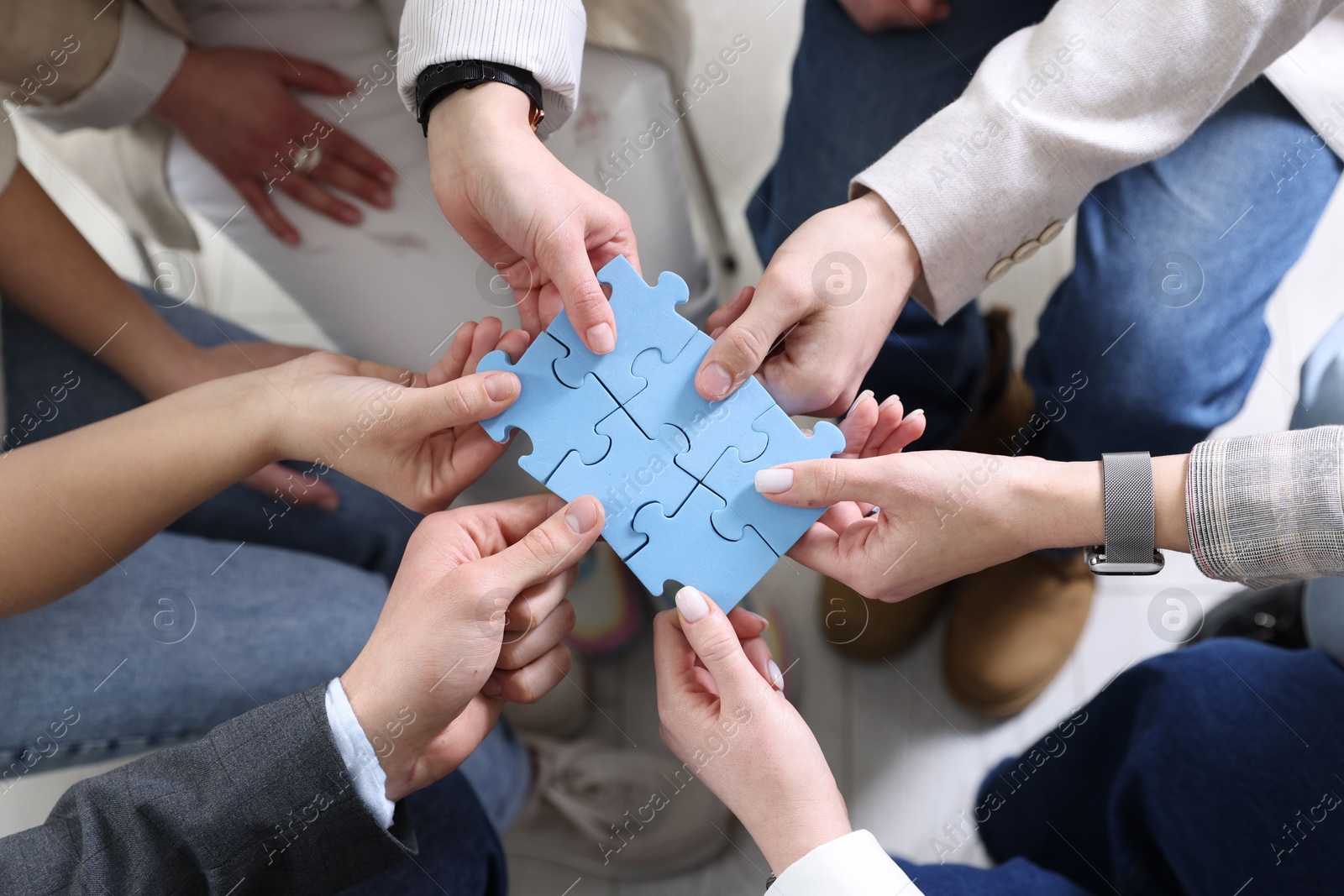 Photo of Unity concept. People putting puzzle pieces together indoors, top view