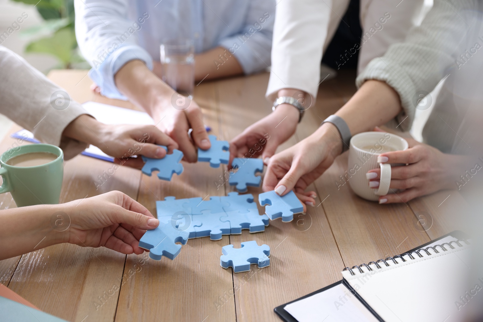 Photo of Unity concept. People putting puzzle pieces together at wooden table indoors, closeup