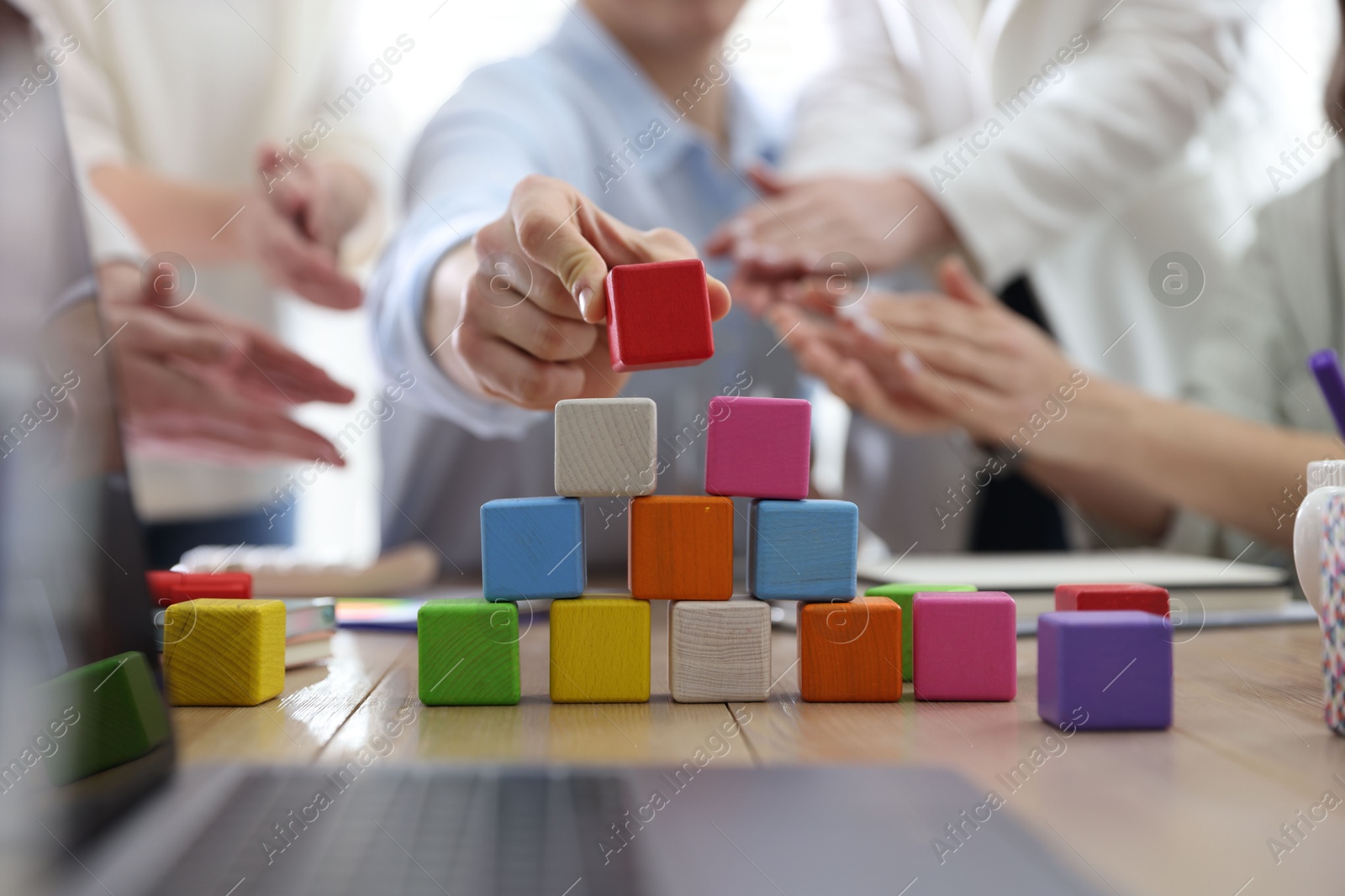 Photo of Unity concept. People building pyramid of colorful cubes at table indoors, closeup