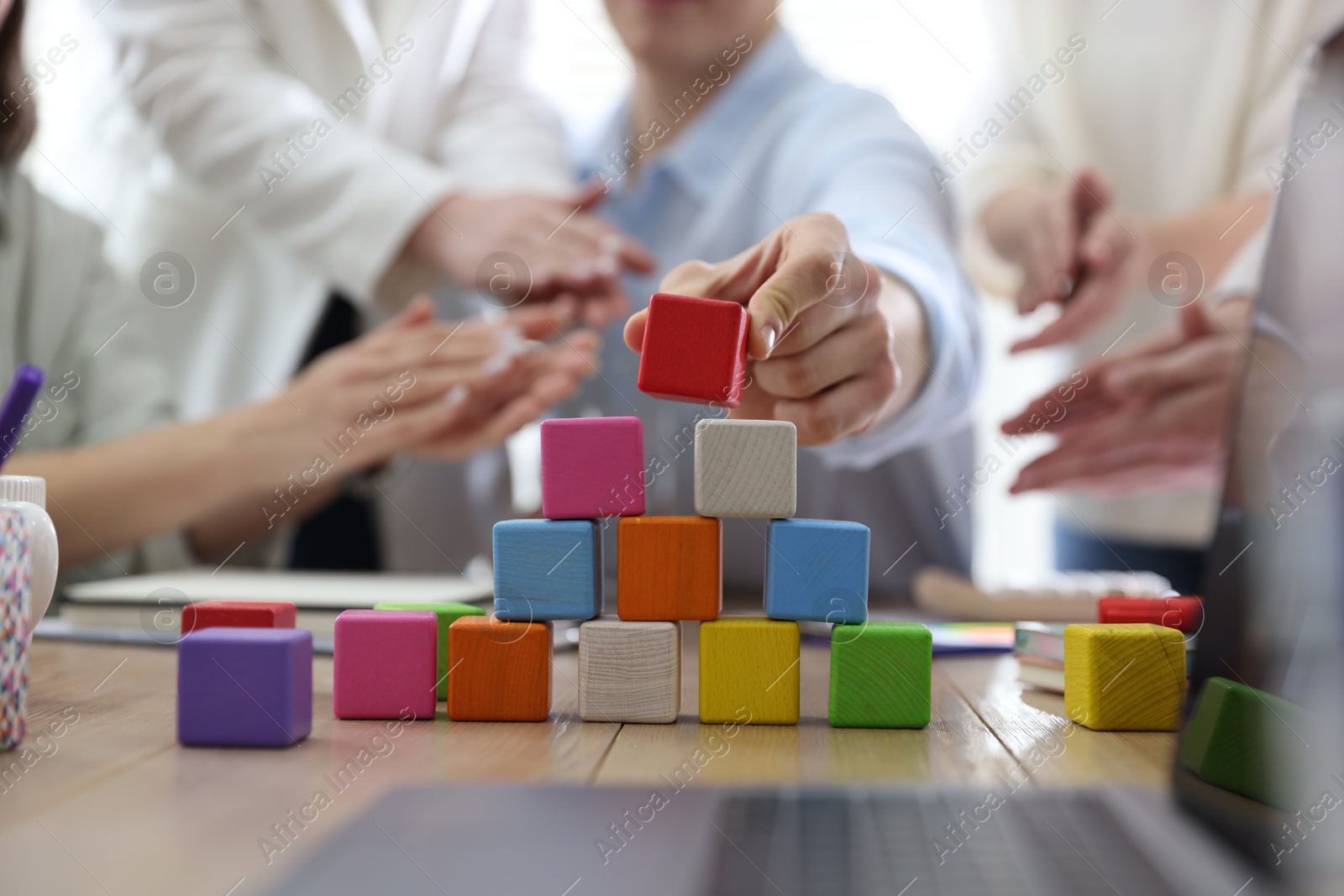 Photo of Unity concept. People building pyramid of colorful cubes at table indoors, closeup