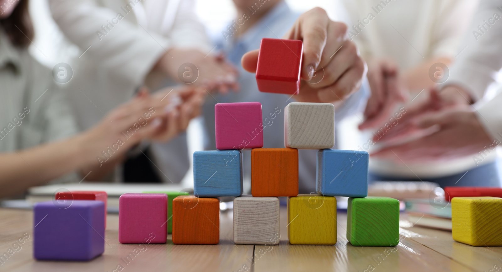 Photo of Unity concept. People building pyramid of colorful cubes at wooden table indoors, closeup