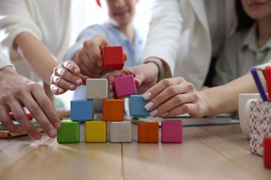 Photo of Unity concept. People building pyramid of colorful cubes at wooden table indoors, closeup