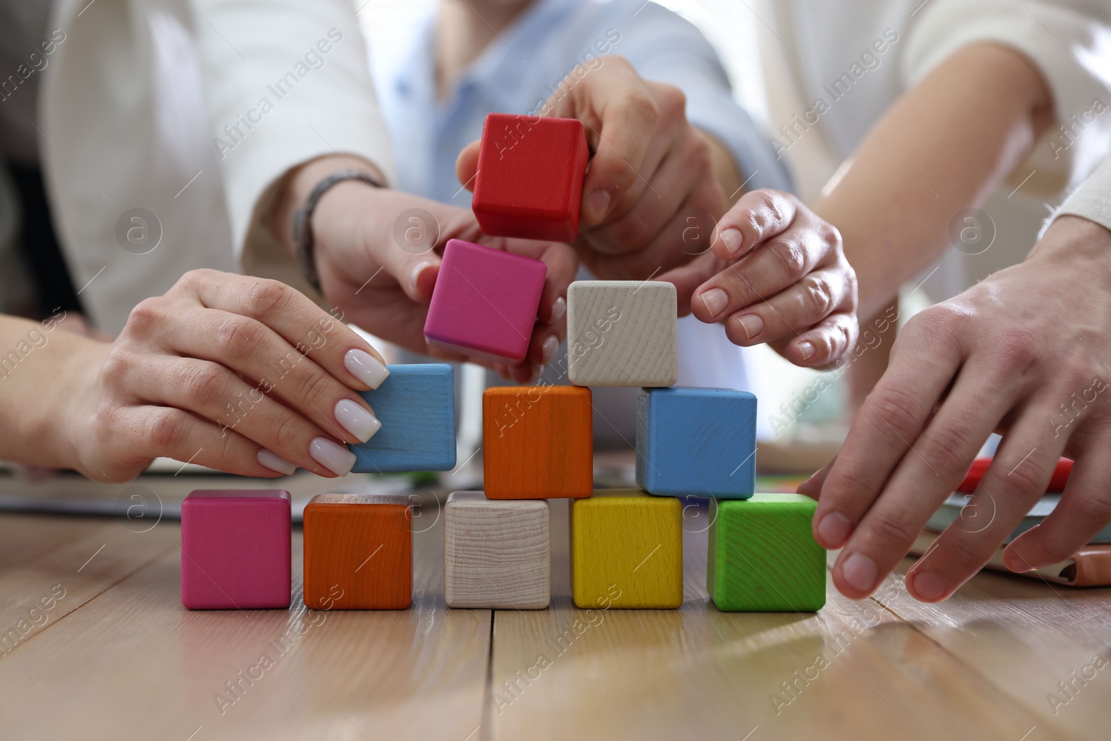 Photo of Unity concept. People building pyramid of colorful cubes at wooden table indoors, closeup