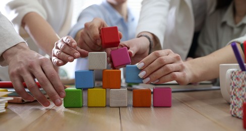 Photo of Unity concept. People building pyramid of colorful cubes at wooden table indoors, closeup