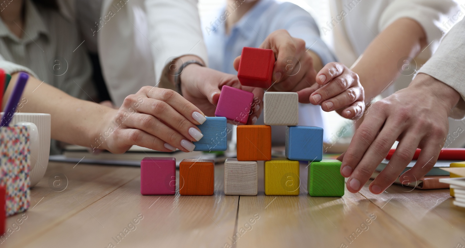 Photo of Unity concept. People building pyramid of colorful cubes at wooden table indoors, closeup