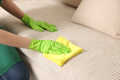 Photo of Janitor cleaning sofa with rag at home, closeup