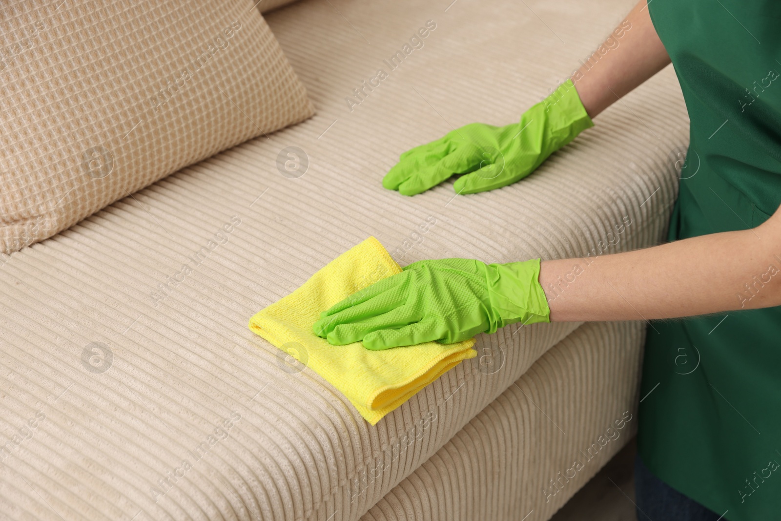 Photo of Janitor cleaning sofa with rag at home, closeup