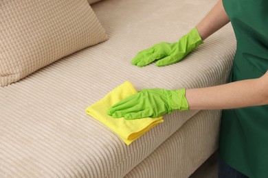 Photo of Janitor cleaning sofa with rag at home, closeup