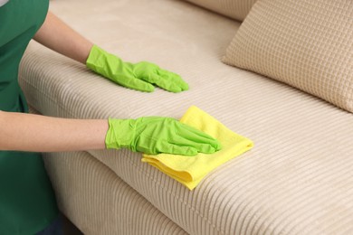 Photo of Janitor cleaning sofa with rag at home, closeup