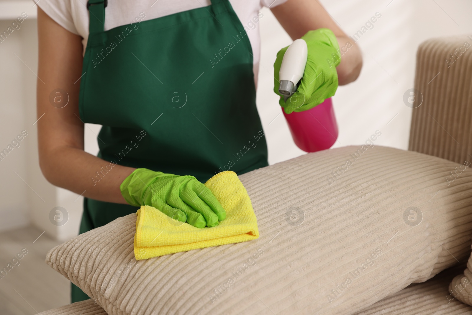 Photo of Janitor cleaning sofa with rag at home, closeup