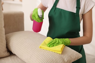 Photo of Janitor cleaning sofa with rag at home, closeup