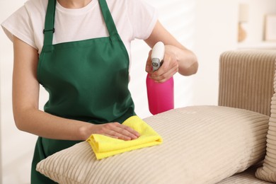 Photo of Janitor cleaning sofa with rag at home, closeup