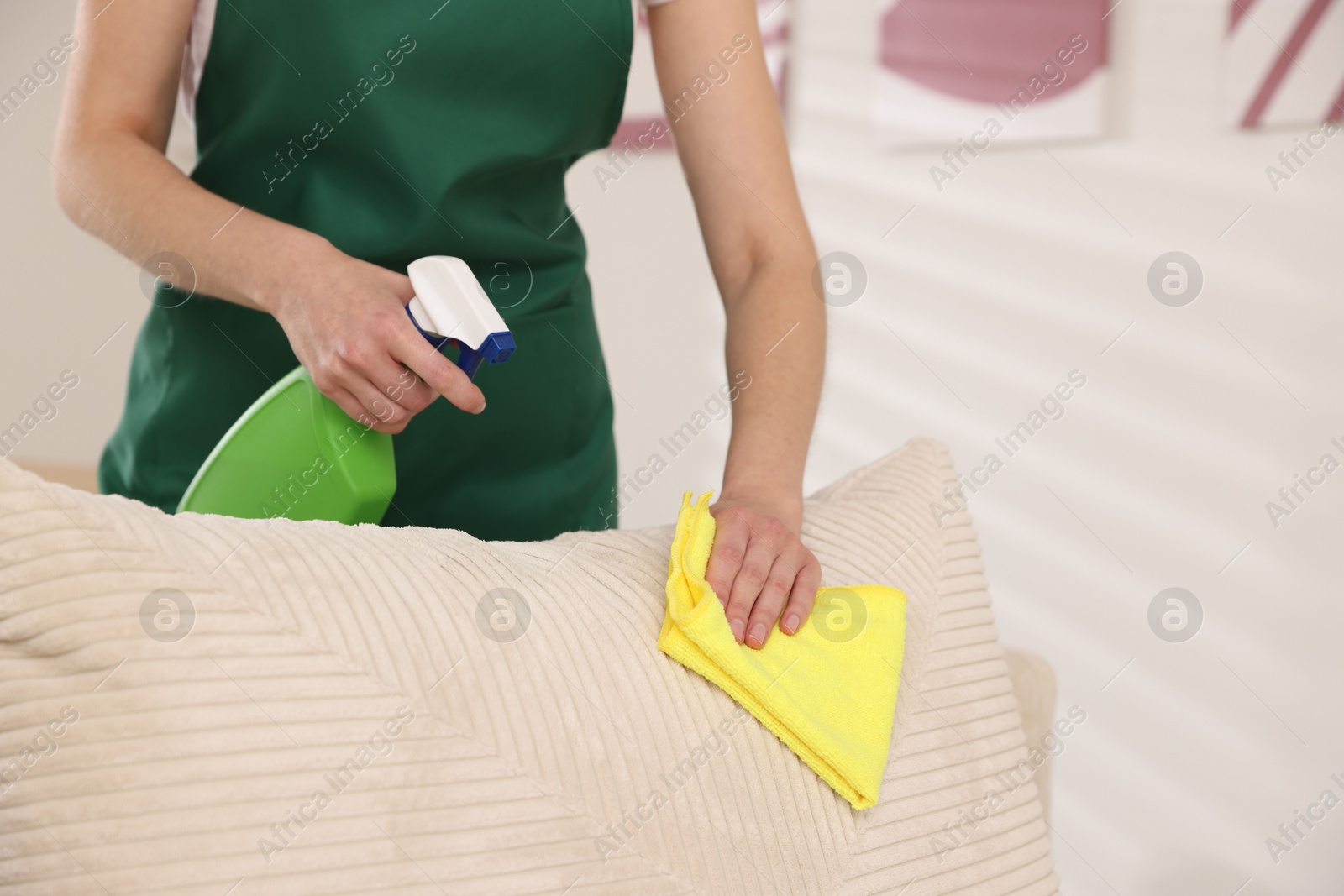 Photo of Janitor cleaning sofa with rag at home, closeup