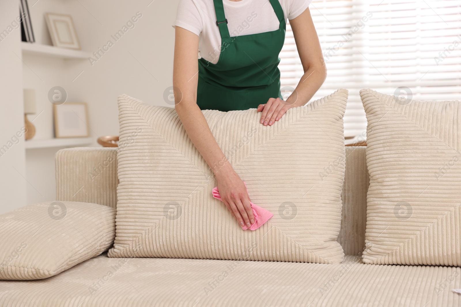 Photo of Janitor cleaning sofa with rag at home, closeup