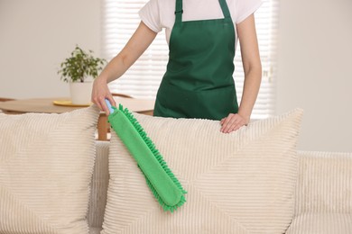 Photo of Janitor cleaning sofa with duster at home, closeup