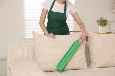 Photo of Janitor cleaning sofa with duster at home, closeup