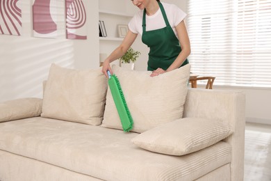 Photo of Janitor cleaning sofa with duster at home, closeup