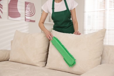 Photo of Janitor cleaning sofa with duster at home, closeup